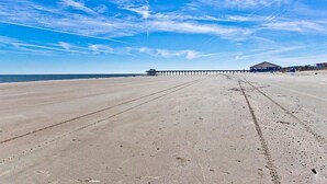 A beach with a long pier extending into the ocean, a clear sky, and a few buildings in the distance. - Butler Beach Cottage by Tybee Vacation Rentals (Tybee Island)