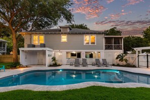 Une maison à deux étages avec une piscine, un patio couvert avec des chaises et une cour arrière clôturée.