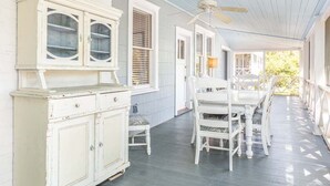 A porch with a white cabinet, a ceiling fan, and a dining table with chairs. - Butler Beach Cottage by Tybee Vacation Rentals (Tybee Island)