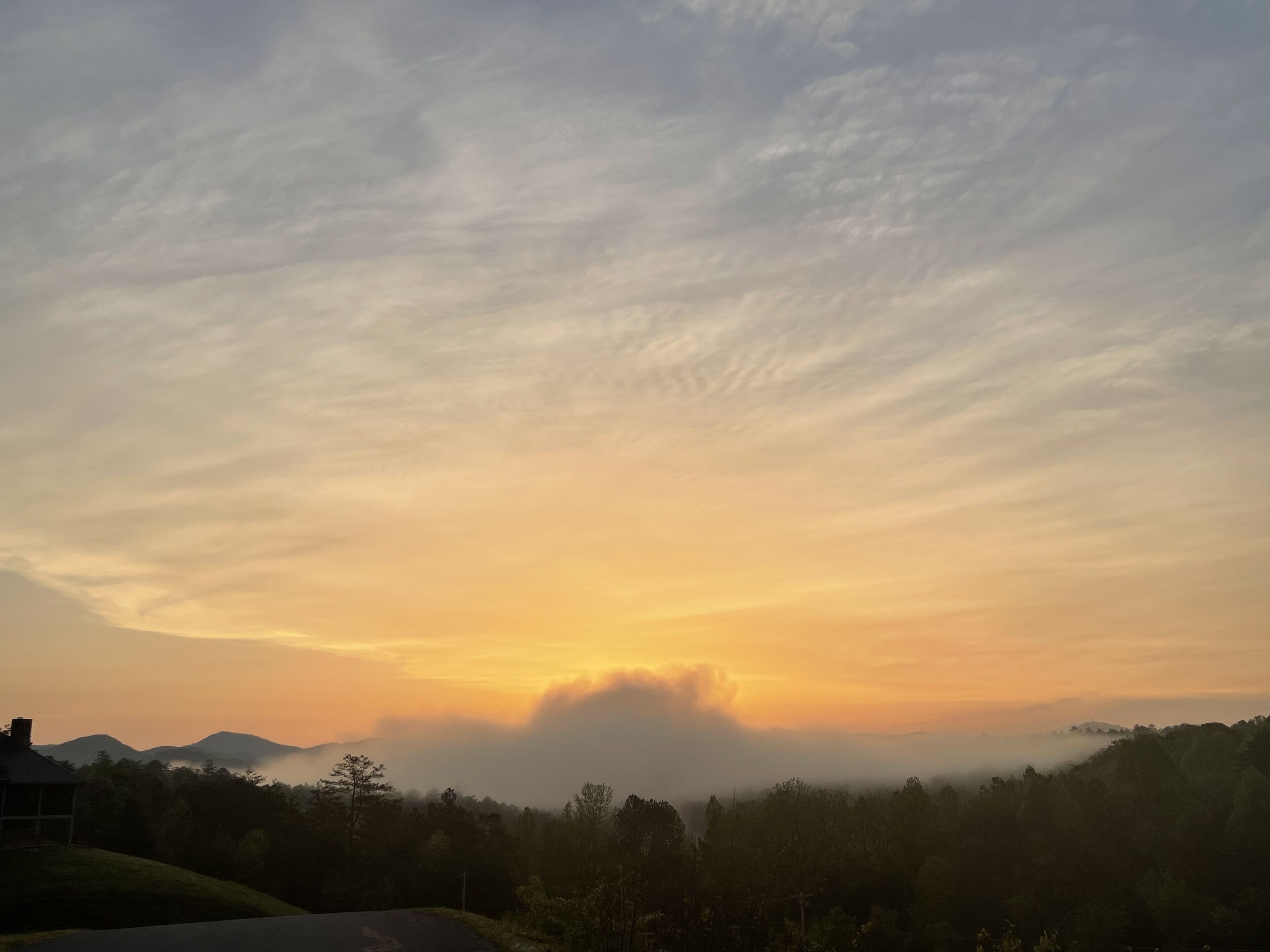 A landscape with a house and trees at sunrise or sunset.