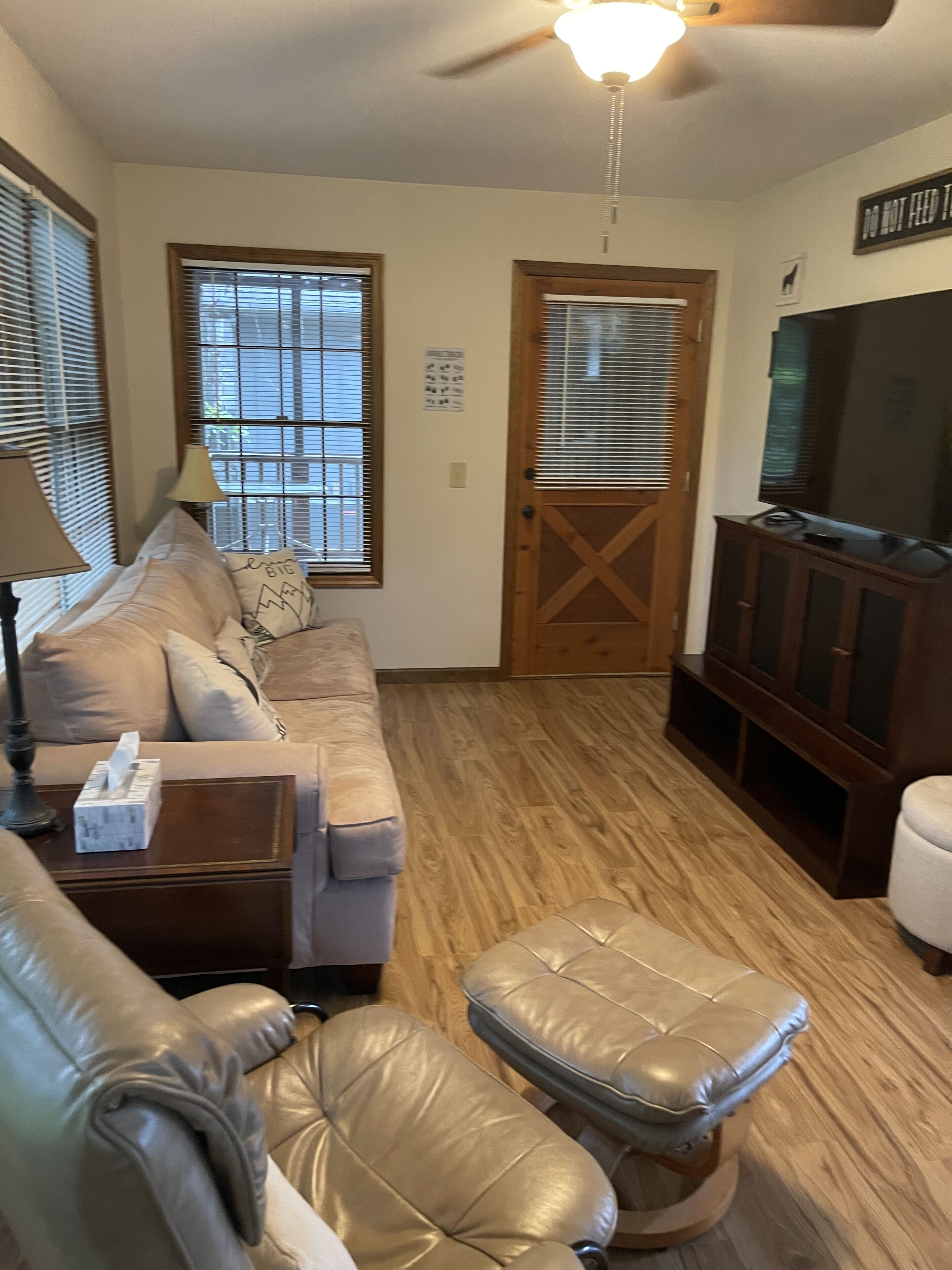 Una sala de estar con sofá, reposapiés, aparador de madera y televisor.