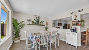Un coin repas avec une table et des chaises, une cuisine en arrière-plan et une enseigne indiquant « Café et thé ».
