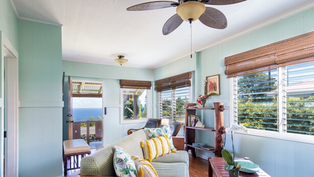 A cozy living room with a sofa, a wooden bench, and a table with a plant. There are windows with blinds and a ceiling fan. - Cozy Cottage in Honoka'a with ocean view from front Lani. (Honokaa)