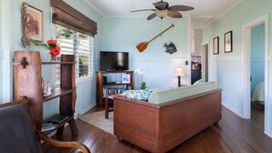A living room with a wooden sofa, a television, a bookshelf, and a ceiling fan. - Cozy Cottage in Honoka'a with ocean view from front Lani. (Honokaa)