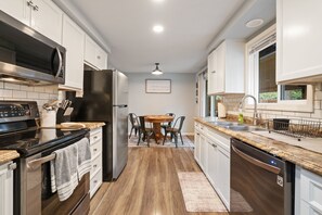 Una cocina moderna con armarios blancos, un refrigerador negro, un microondas, un lavavajillas y un comedor con una mesa y sillas.