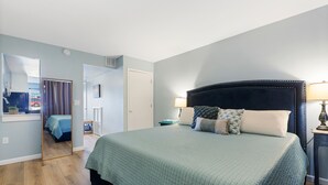 Une chambre à coucher comprenant un lit, des tables de chevet, un miroir et une porte donnant sur une autre pièce.