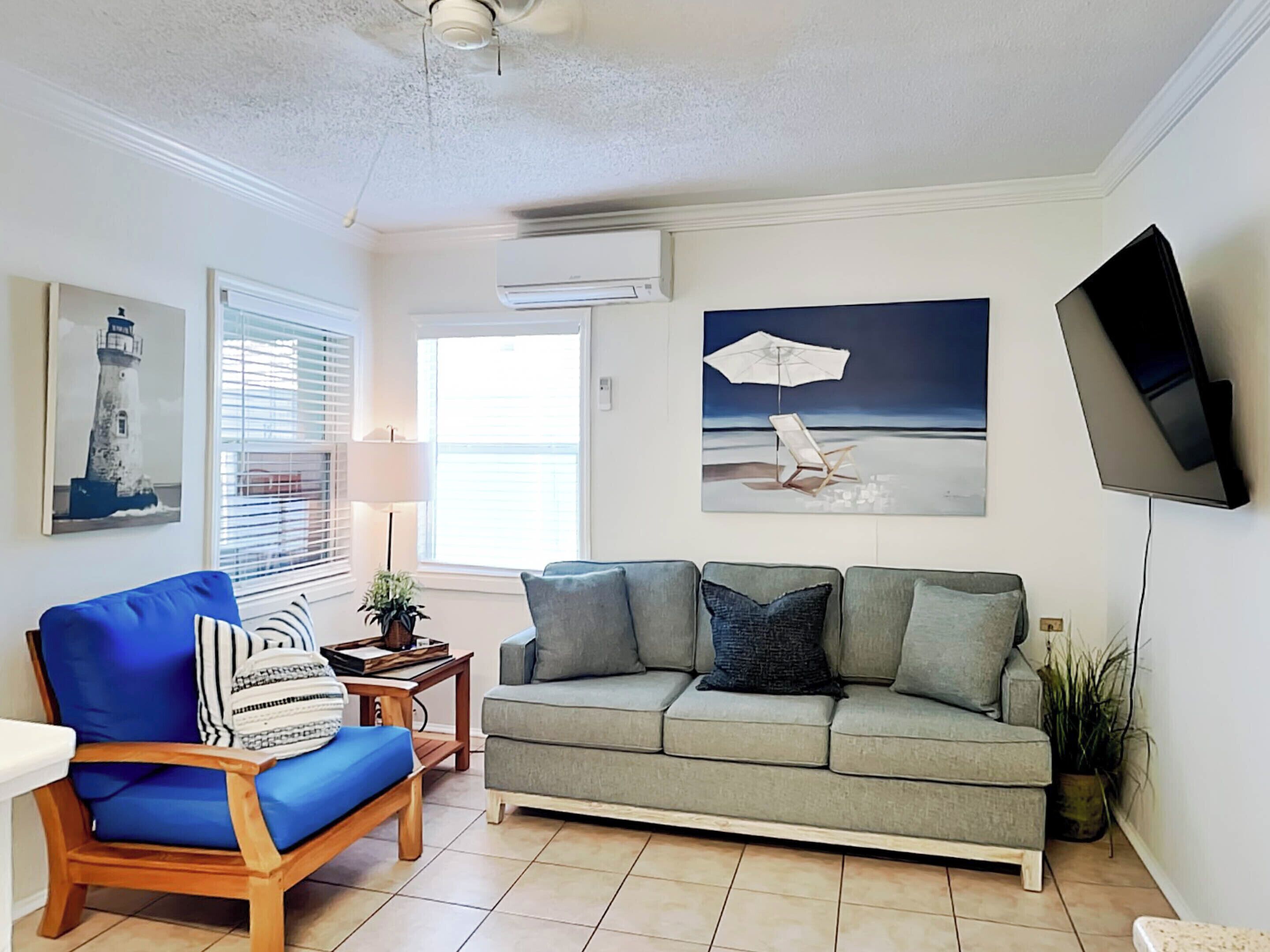A living room with a blue armchair, grey sofa, and a flat-screen TV mounted on the wall.