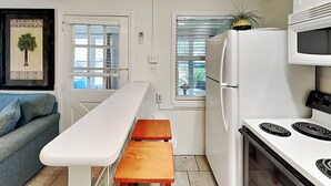 Una cocina compacta con encimera blanca, un banco de madera, un refrigerador blanco, un microondas y una estufa.