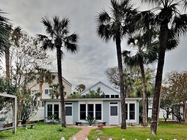 A two-story house with a front porch, surrounded by palm trees and a well-maintained lawn.
