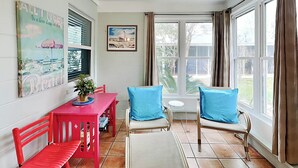 Un comedor con una mesa y sillas rojas, una planta en maceta y vistas al exterior a través de amplios ventanales.