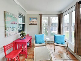 A dining area with a red table and chairs, a potted plant, and a view of the outdoors through large windows.