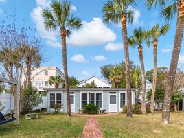 A single-story house with a brick pathway leading to the front door, surrounded by palm trees and a clear blue sky.