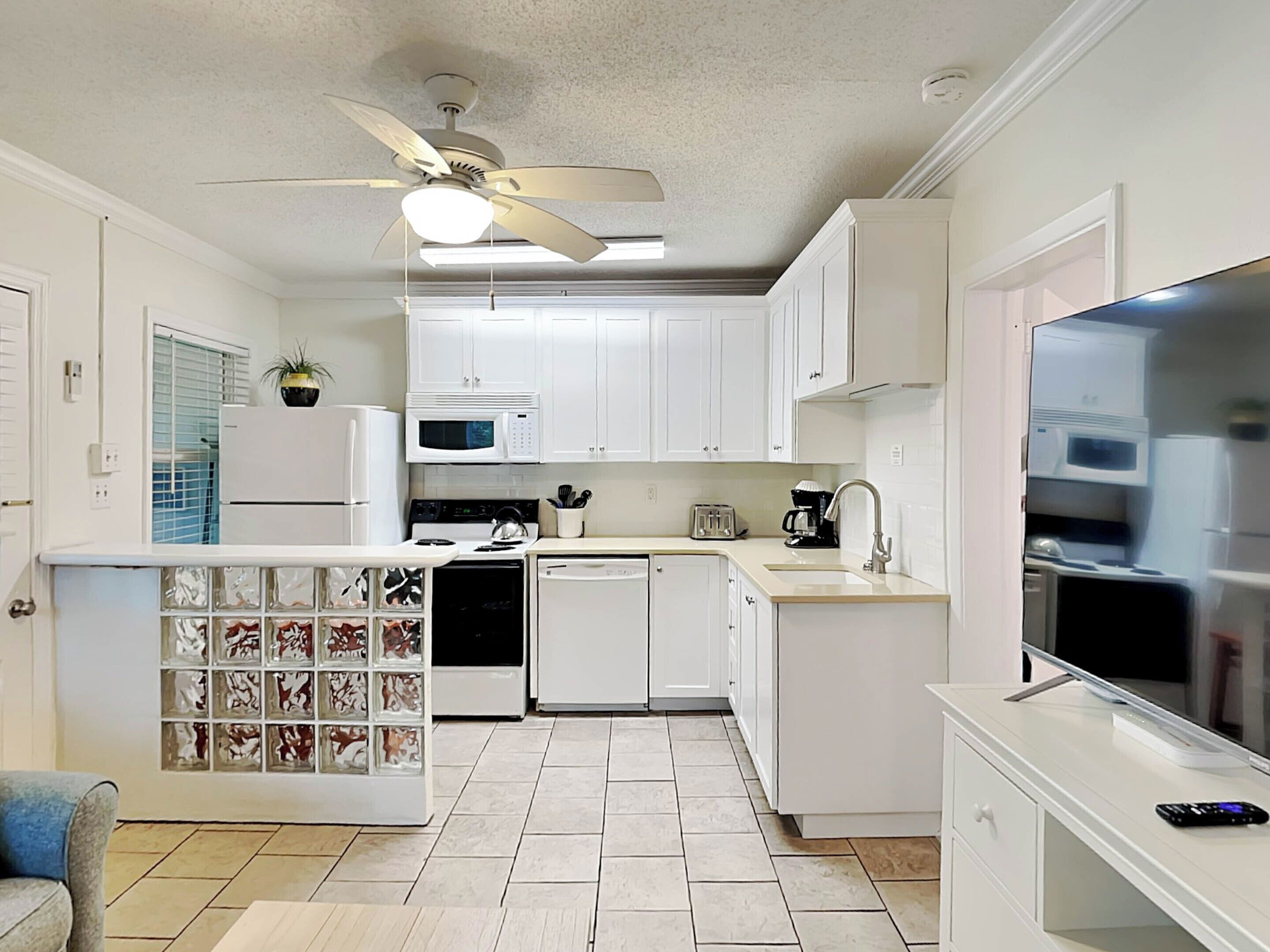 Une cuisine de taille réduite avec des meubles blancs, un four à micro-ondes, une cuisinière, un lave-vaisselle et un ventilateur de plafond.
