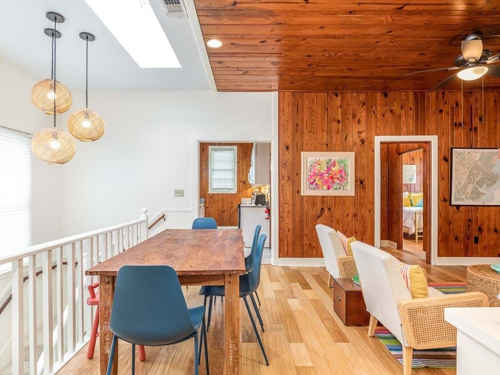 A spacious room with a wooden ceiling, a dining table with chairs, a sofa, and a ceiling fan.
