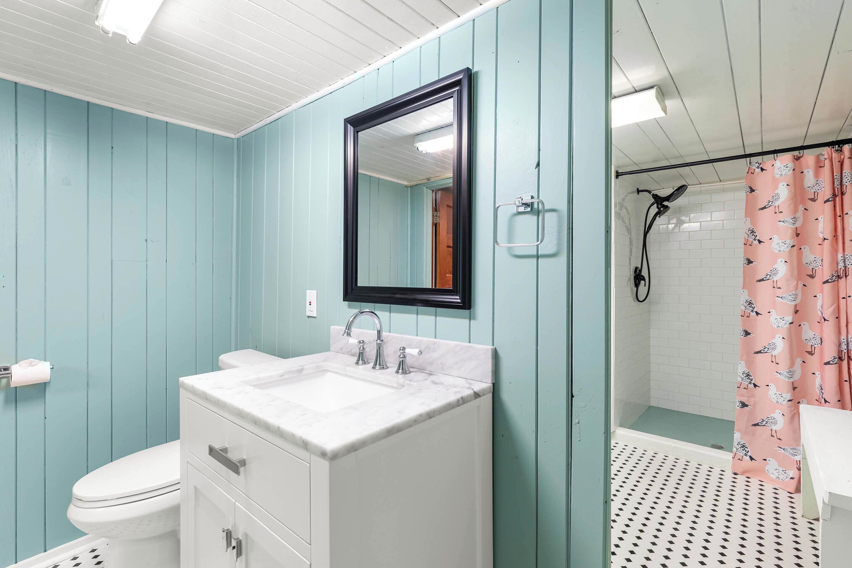 A bathroom with teal walls, a white sink with a marble countertop, a white toilet, and a shower with a pink seagull-patterned curtain.