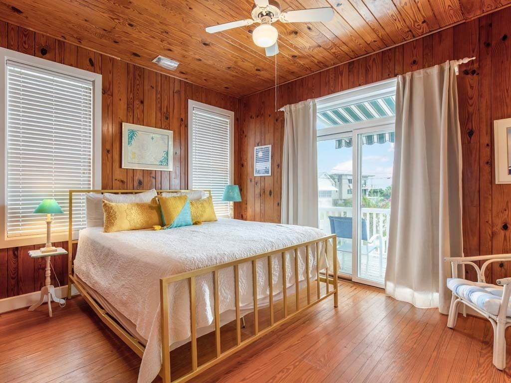 A wooden-paneled bedroom with a bed, a ceiling fan, and a view through a sliding glass door.