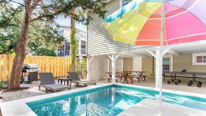 En trädgård med en pool, en grill och en täckt uteplats med ett färgglatt parasoll.