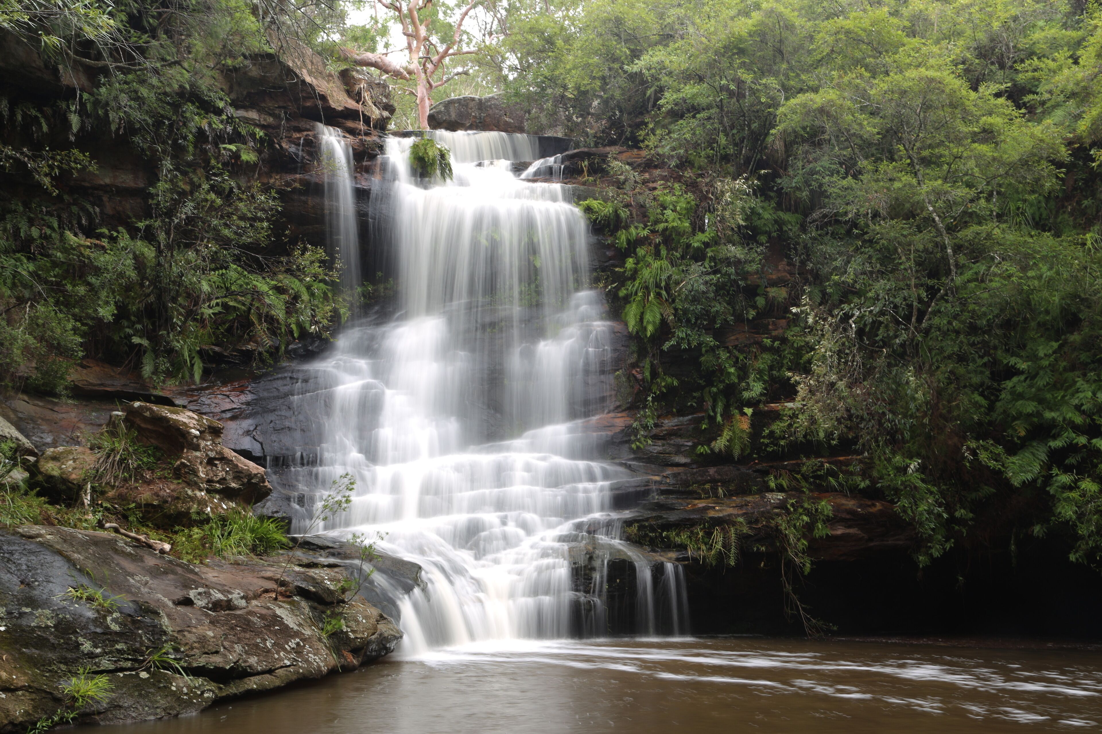 A waterfall cascading over rocky terrain surrounded by dense green foliage.