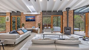 Una sala de estar moderna con pared de ladrillo, chimenea y grandes ventanales con vistas al exterior.