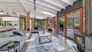 Una sala de estar moderna con chimenea, un sofá, una mesa de centro y una cocina visible a través de puertas de vidrio.