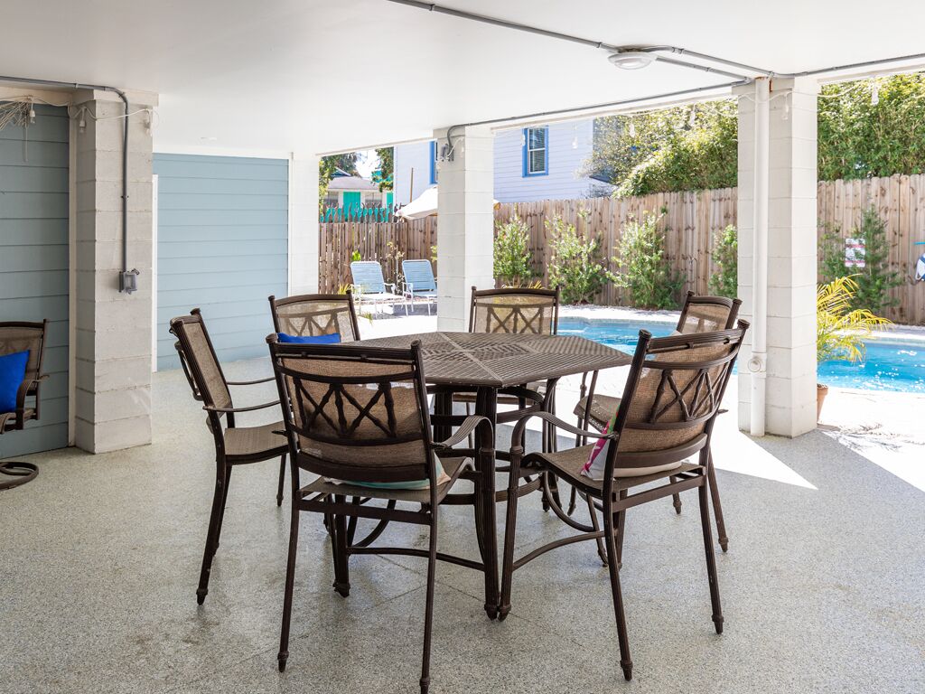 An outdoor patio with a table and chairs, a pool in the background, and a wooden fence.