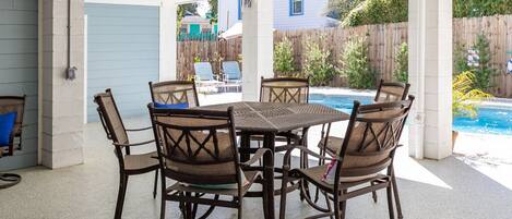 An outdoor patio with a table and chairs, a pool in the background, and a wooden fence.