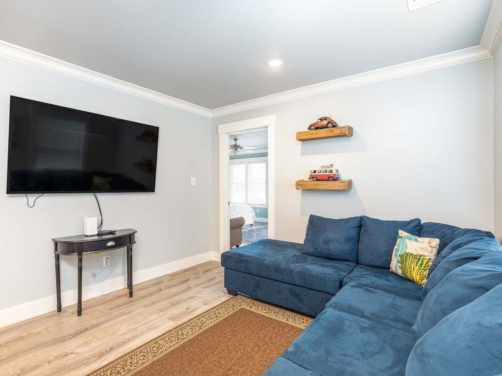 A living room with a blue sofa, a flat-screen TV mounted on the wall, a small wooden side table, and a patterned rug.