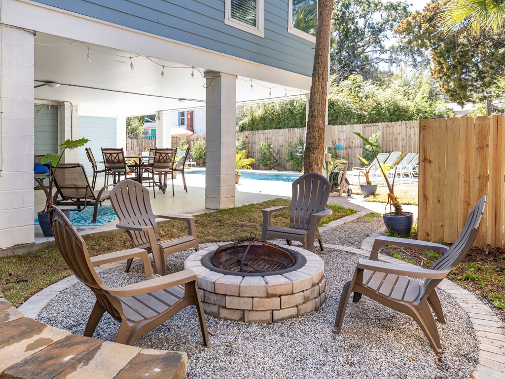 An outdoor patio with a fire pit, seating area, and a view of a swimming pool.