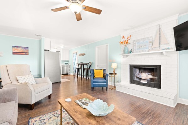 A living room with a fireplace, a ceiling fan, and a dining area with a table and chairs.