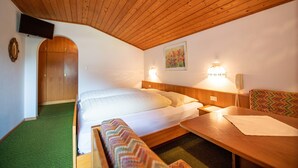Una habitació d'hotel amb sostre de fusta, un llit amb roba blanca, una banca, una taula i un quadre a la paret.