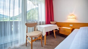A hotel room with a bed, a small table with chairs, a nightstand, and a wall-mounted lamp.