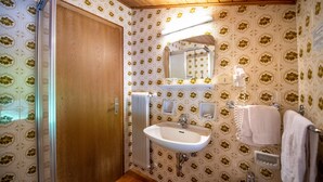 Une salle de bain avec une porte en bois, un lavabo blanc, un miroir et un papier peint à motifs.