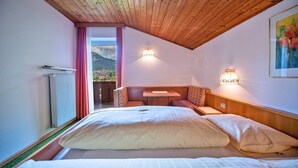Une chambre avec un grand lit, un plafond en bois, une vue sur les montagnes, une petite table et deux lampes fixées au mur.