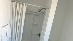 Een kleine, witte badkamer met een douche, toilet en een handdoekrek.
