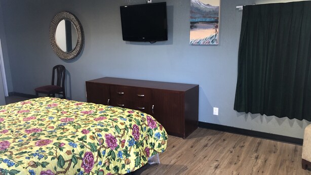 Een slaapkamer met een bed, een dressoir, een stoel, een ronde tafel, een spiegel, een televisie en een schilderij aan de muur.