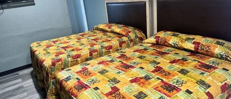 Una stanza con due letti, ognuno con una coperta colorata, una televisione a schermo piatto montata a parete e un pavimento in legno.