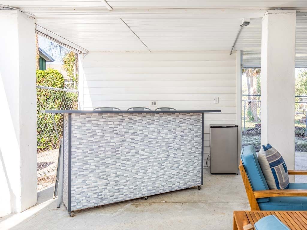 A covered patio area with a brick partition, a small kitchenette, and a seating area with a blue cushion.