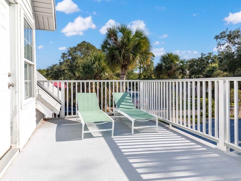 A balcony with two green lounge chairs and a white railing.