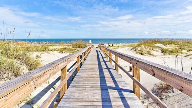 A wooden boardwalk leading to a beach with sand dunes and a clear blue sky. - Catch A Wave by Tybee Vacation Rentals (Tybee Island)