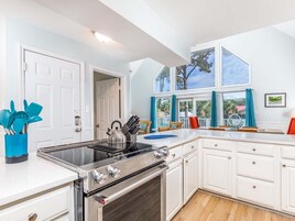 Una cocina moderna con armarios blancos, una estufa de acero inoxidable y un amplio ventanal con cortinas.