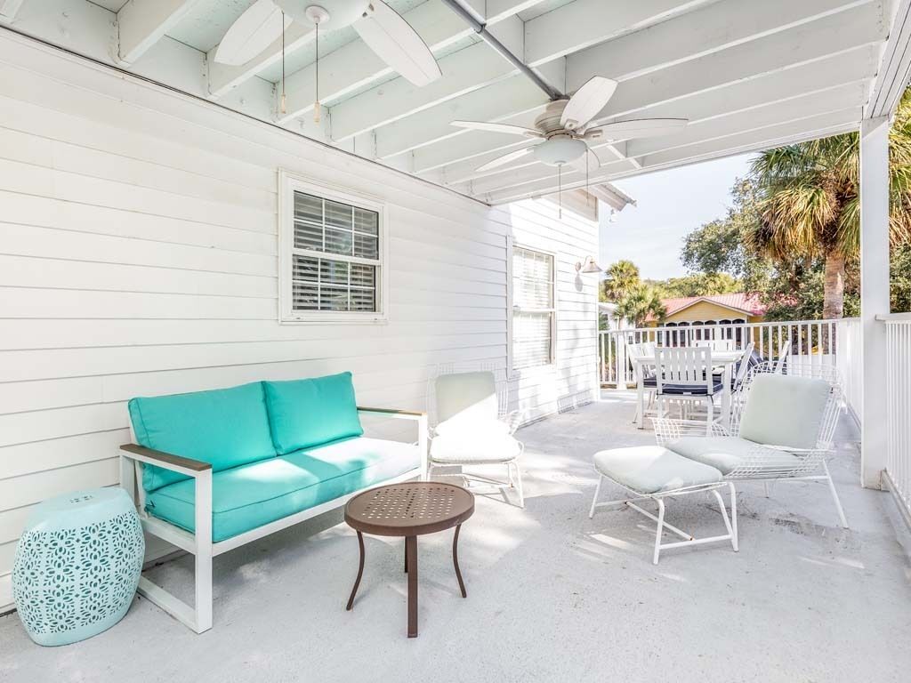 A covered outdoor area with a white wooden structure, a turquoise sofa, white chairs, and a small round table.