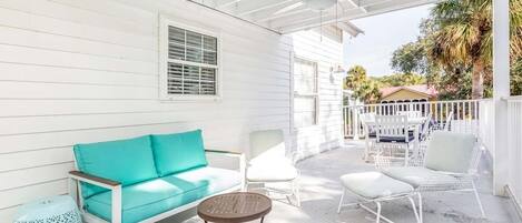 A covered outdoor area with a white wooden structure, a turquoise sofa, white chairs, and a small round table.