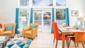 A spacious living room with a high ceiling, large windows, and a balcony. There are two sofas, a dining table, and a coffee table. - Catch A Wave by Tybee Vacation Rentals (Tybee Island)