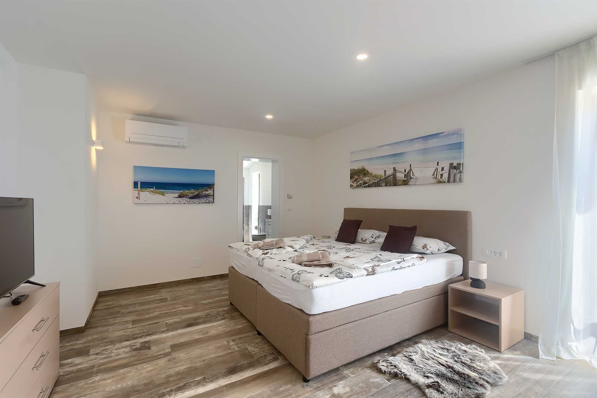 A bedroom with a bed, a bedside table, a TV, and artwork on the walls.