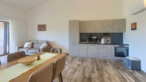 A modern kitchen with grey cabinets, a black countertop, and a built-in oven. There is a dining area with a wooden table and chairs, and a sofa in the background. - Brand New Modern apartment for 4+2 guests with shared pool (Novigrad)