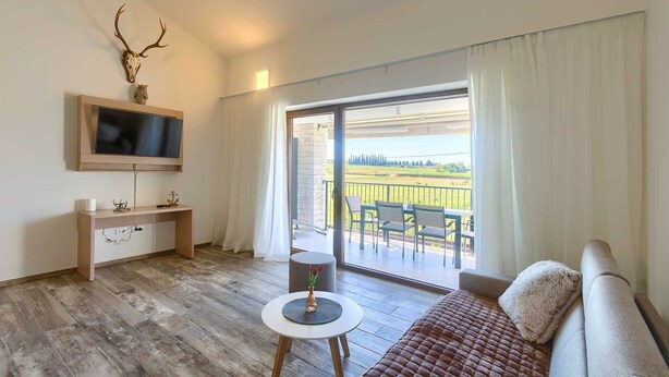 A living room with a sofa, a small round table with a vase, a mounted TV, and a large window with curtains. - Brand New Modern apartment for 4+2 guests with shared pool (Novigrad)