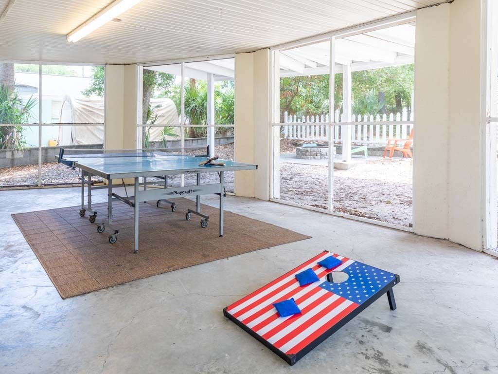 A ping pong table in a covered area with a view of a fenced yard.