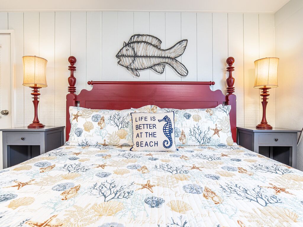 A bedroom with a bed, two bedside tables, a wall-mounted fish artwork, and a pillow with a seahorse design.