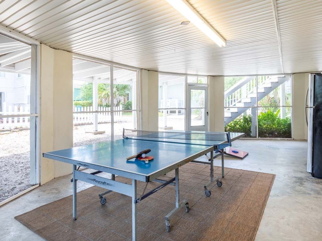 A ping pong table in a covered outdoor area with a view of a staircase and greenery.