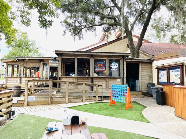 Ein rustikaler Außenbereich mit einer Holzterrasse, einem Picknicktisch und einer blau-orangenen Spielkonstruktion.